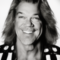 a person with long hair smiling widely, wearing a patterned shirt. black and white image.